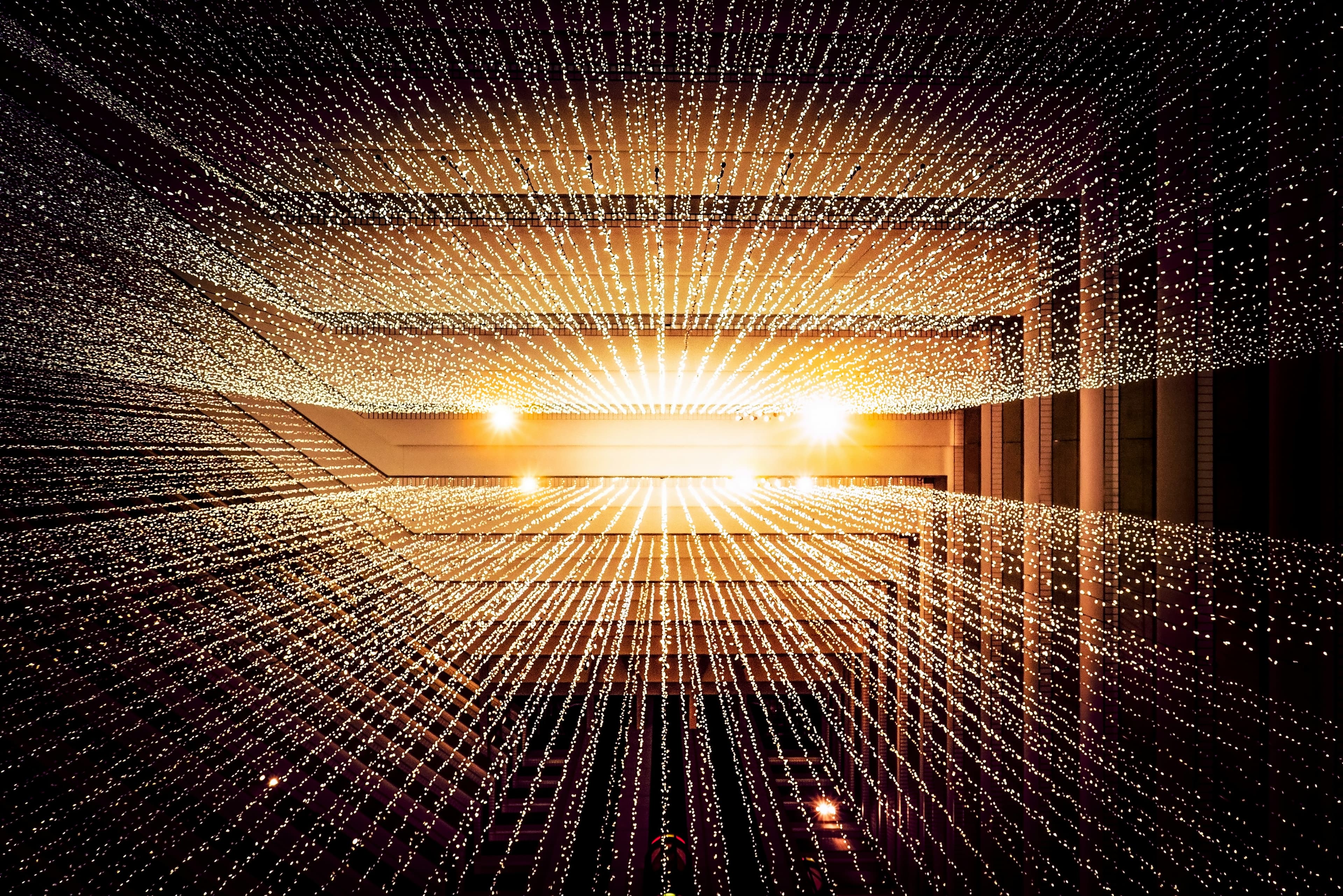 Rows of string lights radiating from a glowing point along the underside of a covered walkway at night
