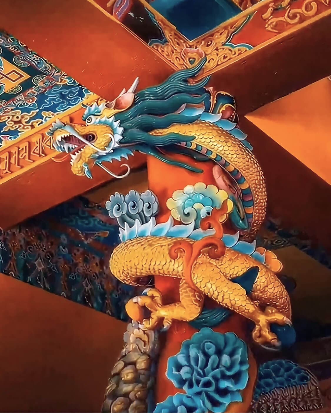 A gilded thunder dragon carved into a temple roof beam, painted in gold and turquoise.